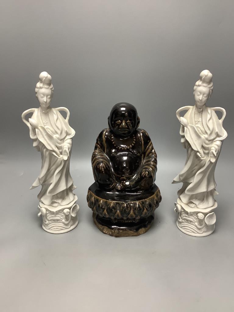 A Chinese dark brown glazed Buddha, and a pair of blanc de chine figures of Guanyin, tallest 30cm